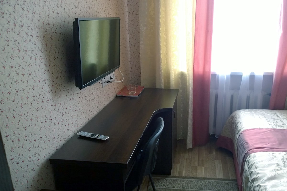Una habitación de hotel con una cama, un escritorio con televisor y una ventana con cortinas.