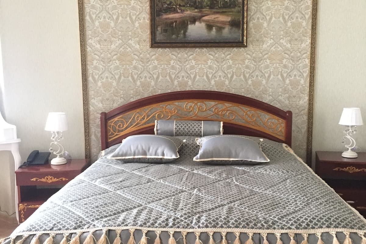 Una cama bien tendida con una colcha estampada y flecos, un cuadro de paisaje enmarcado en la pared, y dos mesitas de noche con lámparas.
