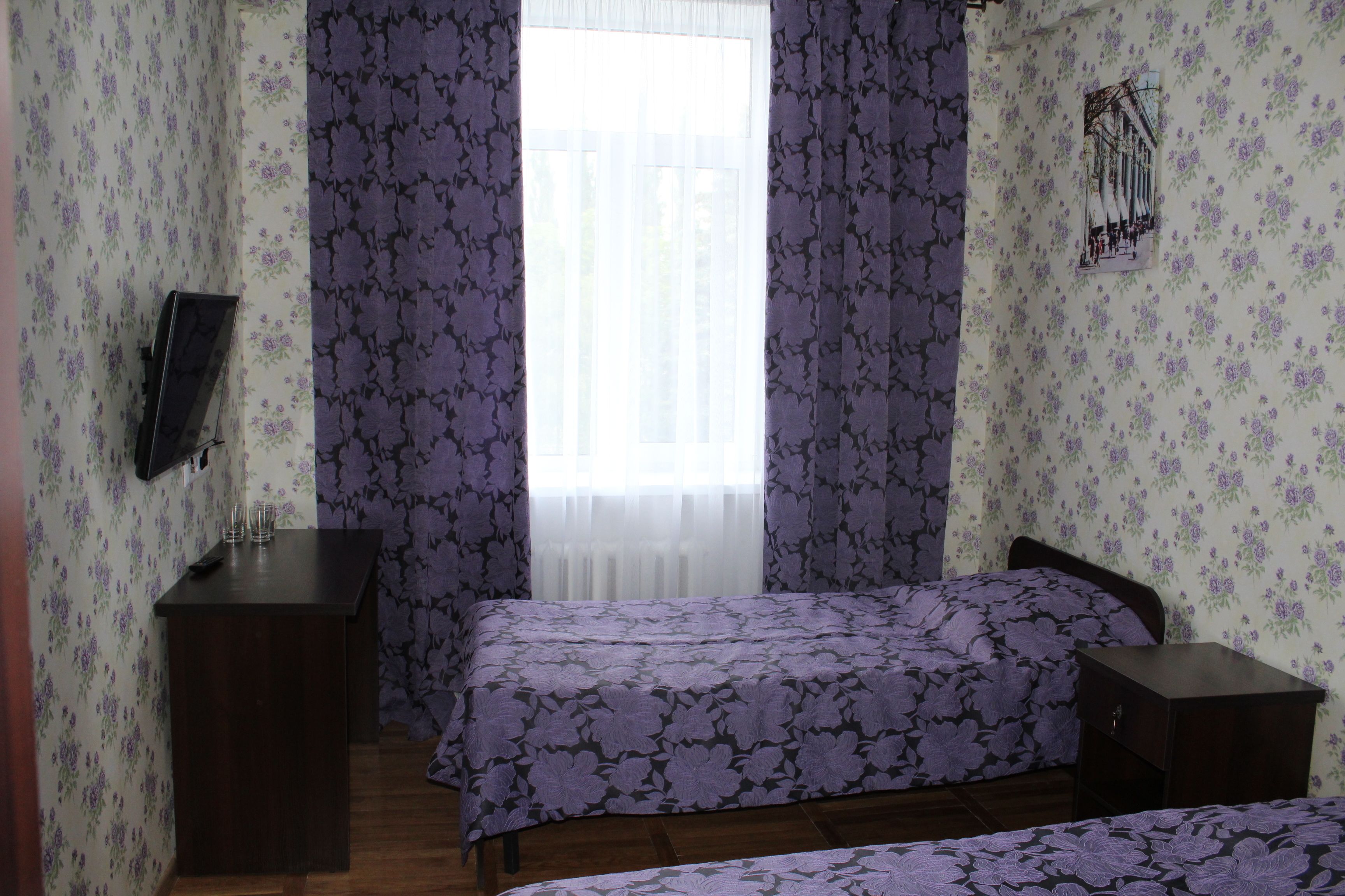 A bedroom with two beds, a TV, and a window with curtains.