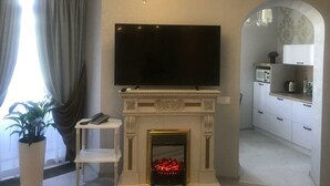 A living room with a flat-screen TV, a fireplace, and a kitchen area with white cabinets and a microwave. - Hotel Bug Brest (Brest)