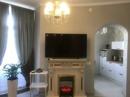 Una sala de estar con televisor de pantalla plana, chimenea y una zona de cocina con armarios blancos y microondas.