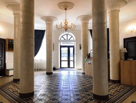Un amplio pasillo con grandes columnas, piso estampado y candelabro.