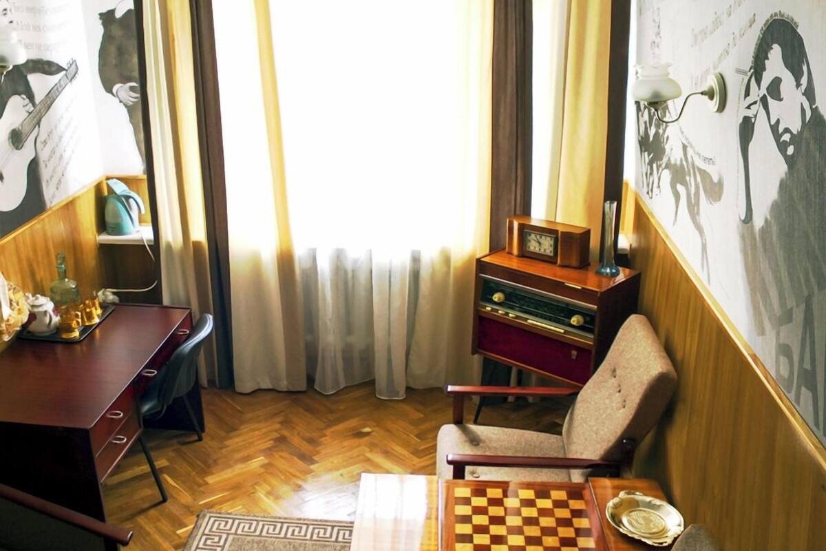 Una habitación con un escritorio de madera, una silla, un tablero de ajedrez, una radio pequeña y un cartel en la pared.