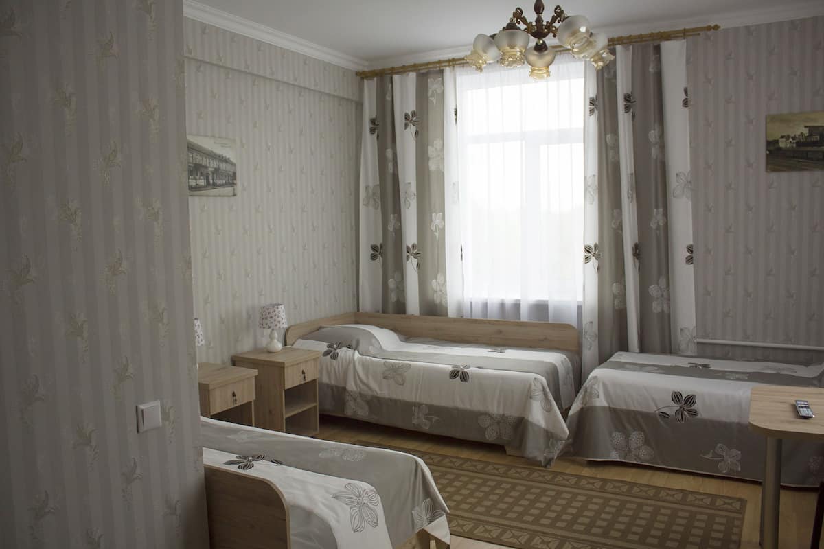 Una habitación de hotel con dos camas individuales, una mesita de noche de madera, una pequeña mesa y una alfombra estampada.