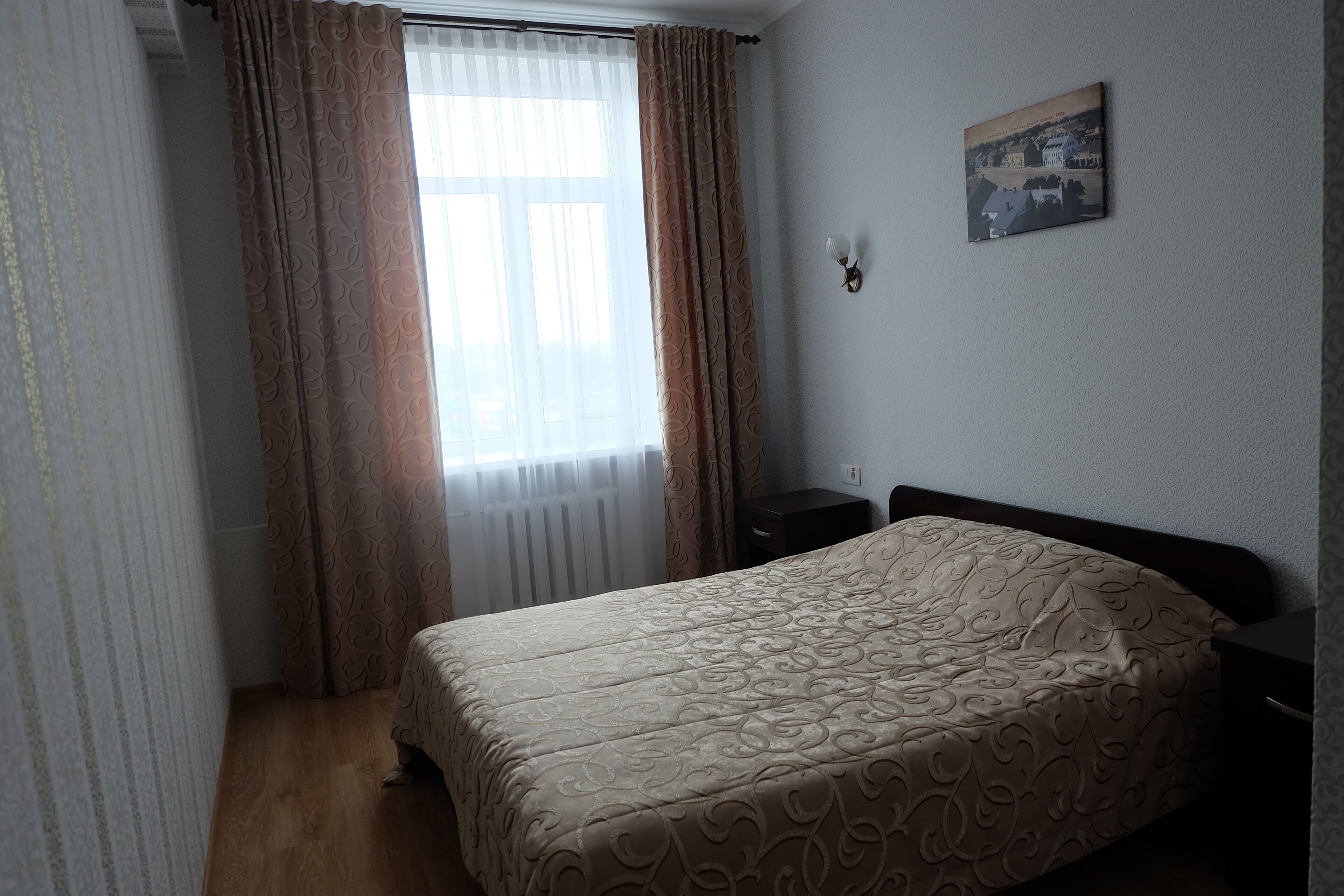 A bedroom with a bed, a nightstand, a wall-mounted light, and a window with curtains.