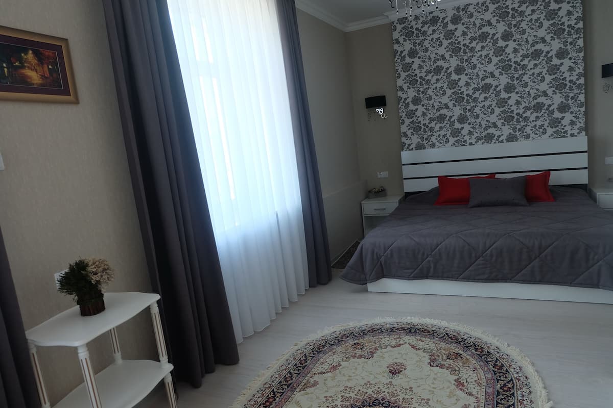 Un dormitorio con cama, mesita de noche, televisor montado en la pared y ventana con cortinas.