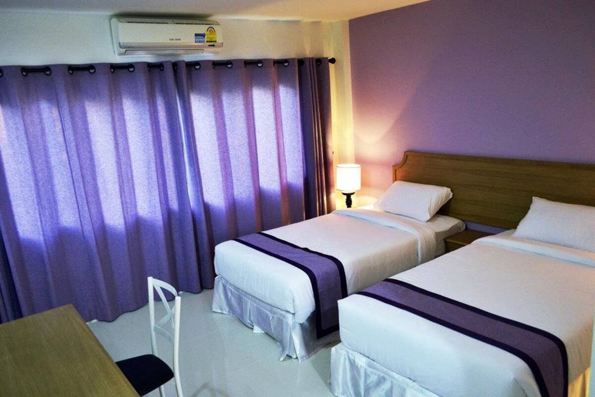A hotel room with two beds, a desk, a chair, and a window with purple curtains.