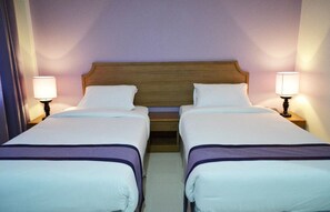 A hotel room with two single beds, each with a wooden headboard, white bedding, and bedside lamps.