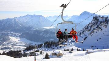 Eine Sesselbahn mit Fahrgästen, schneebedeckte Berge und eine kleine Hütte im Hintergrund.