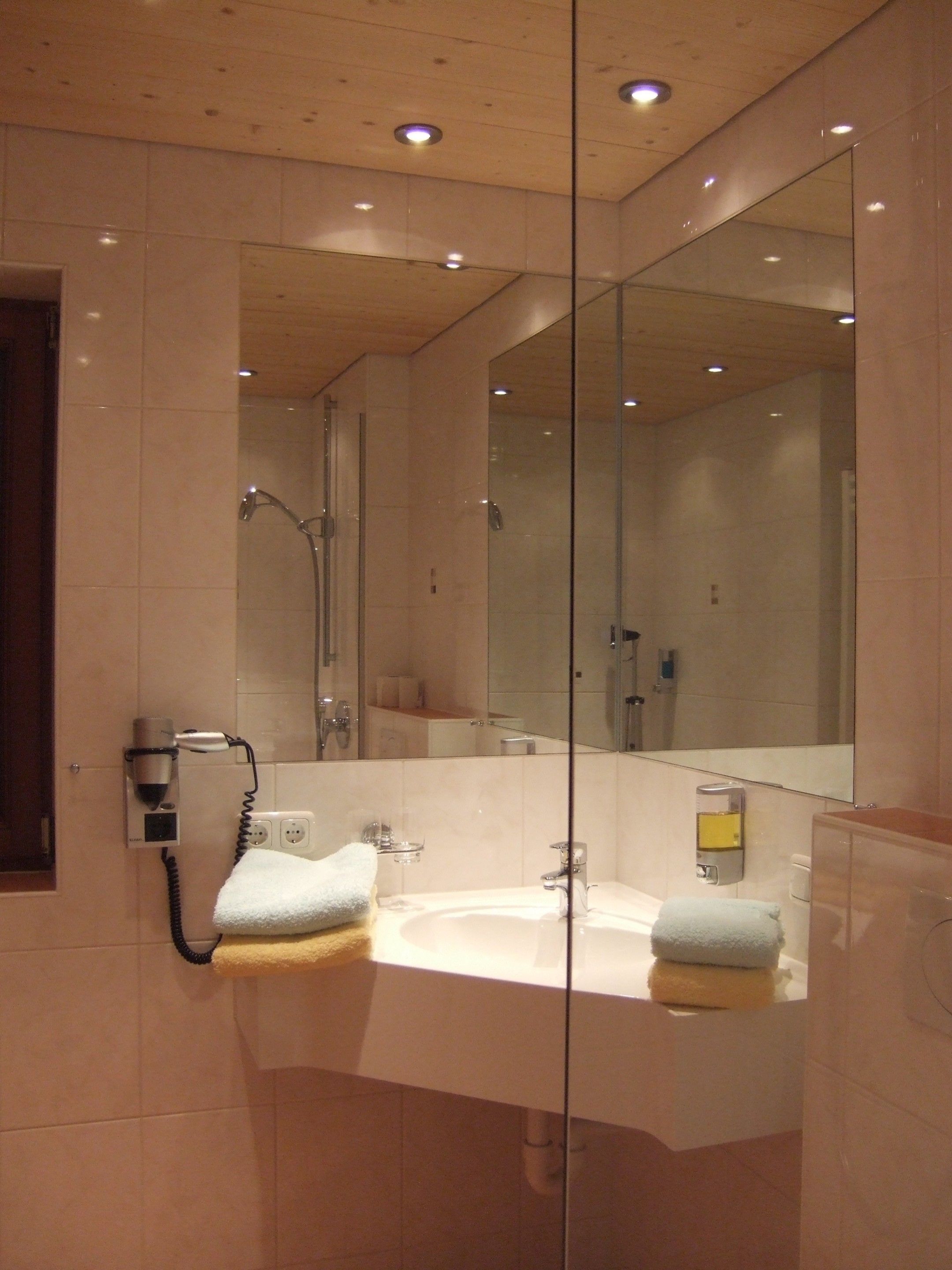Une salle de bain moderne avec un grand miroir, un sèche-cheveux et deux serviettes posées sur le lavabo.