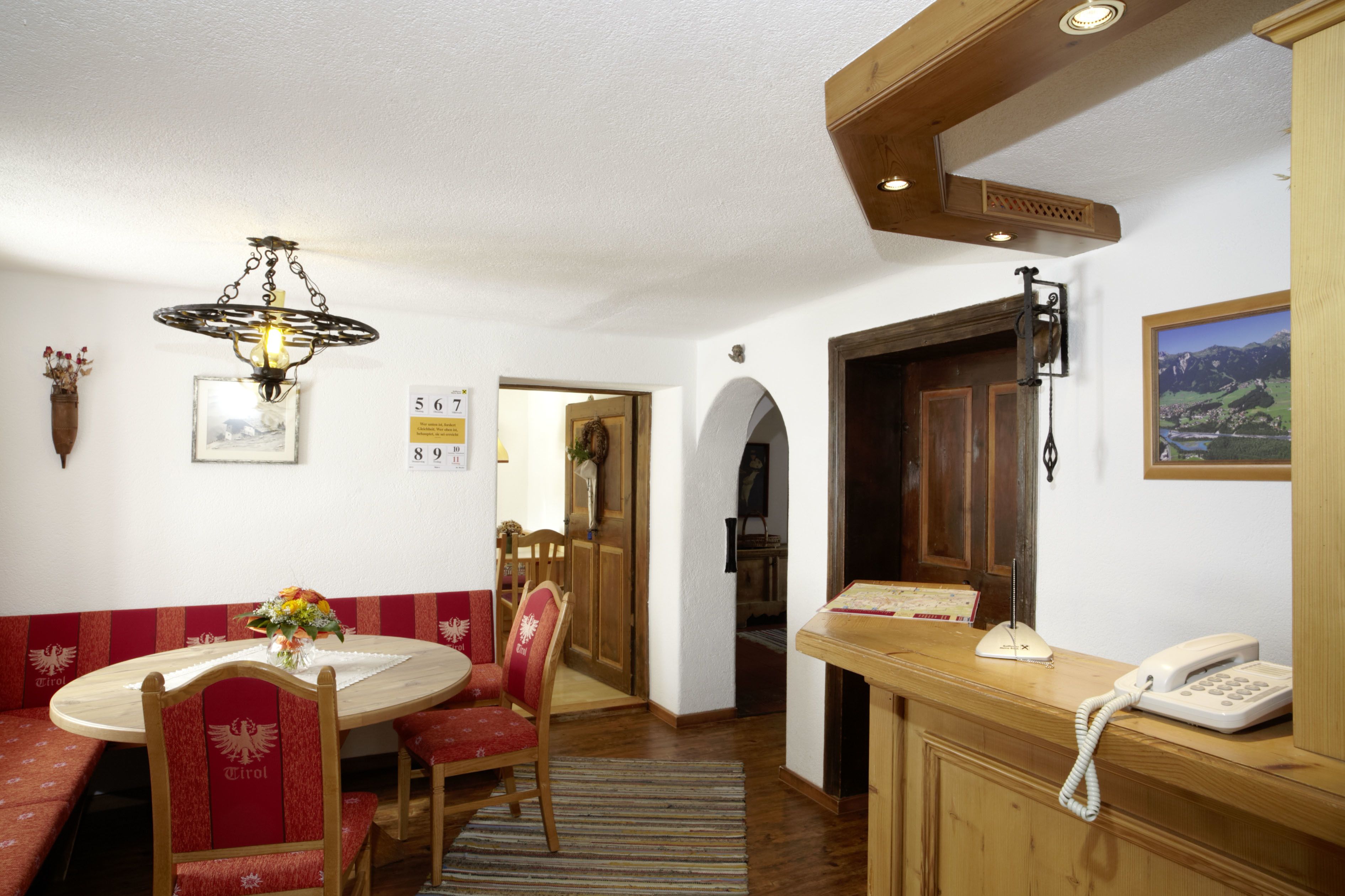 Una habitación de hotel con un mostrador de recepción de madera, un teléfono, un cuadro enmarcado en la pared y un área de comedor con una mesa y sillas.