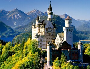 A castle with multiple towers, surrounded by lush greenery and mountains in the background.