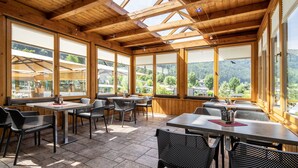 A wooden-paneled dining area with tables and chairs, large windows offering a view of the surrounding landscape. - Wellness Landhaus PARTH (Ossiach)