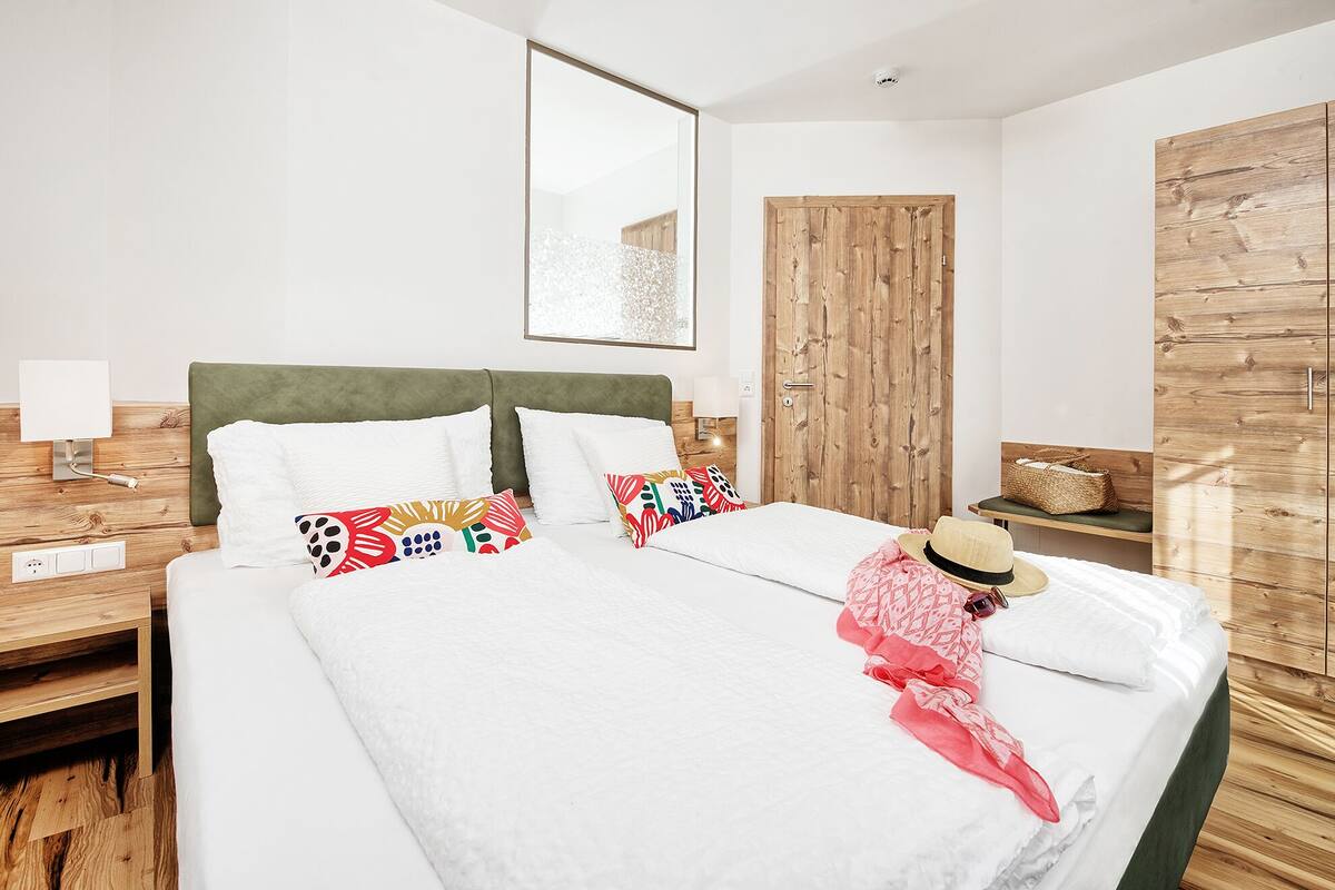 Habitación de hotel con una cama grande, un armario de madera, una mesita de noche con lámpara y un espejo montado en la pared.