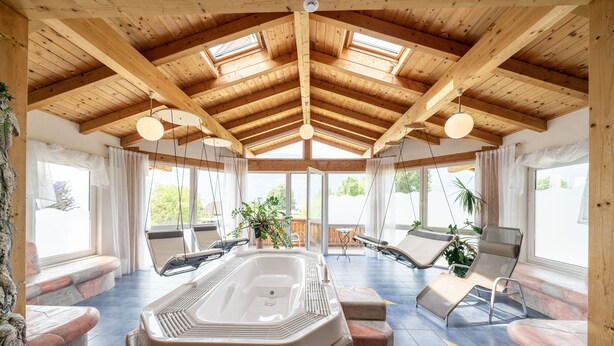 A spa area with a hot tub, lounge chairs, and large windows. - Wellness Landhaus PARTH (Ossiach)