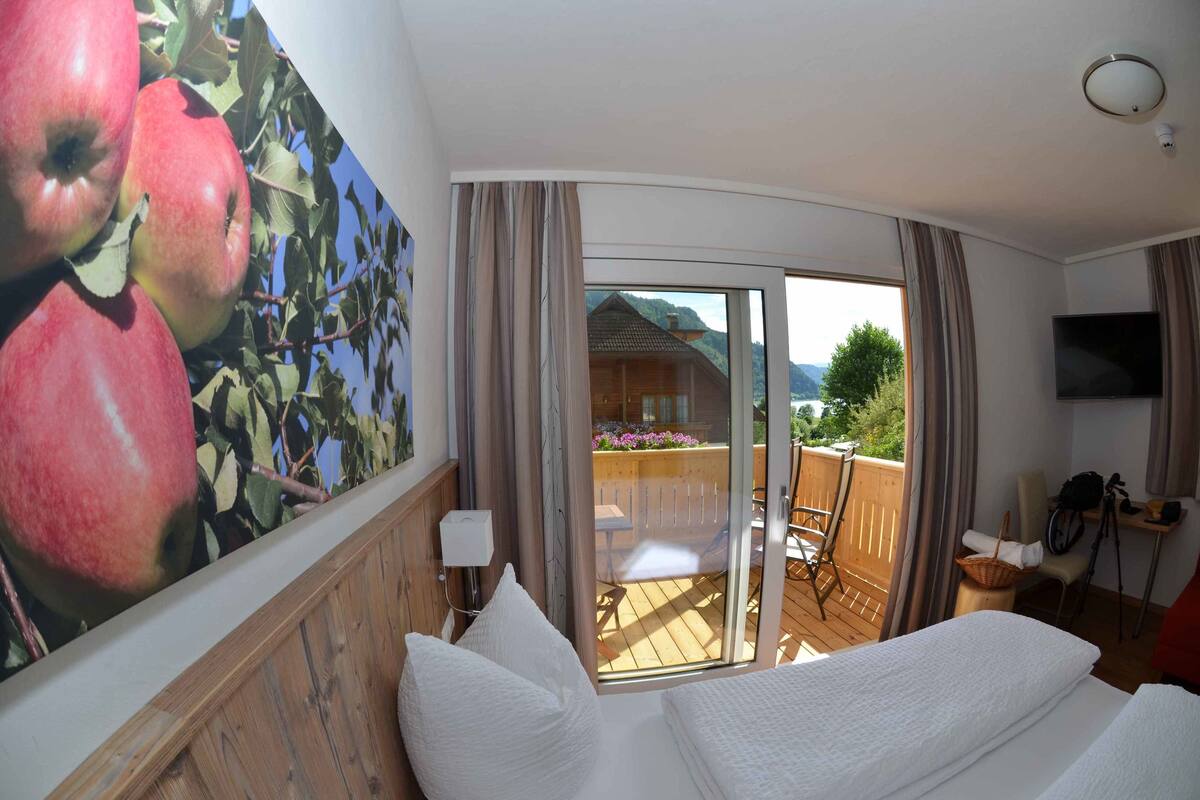 Habitación de hotel con un cuadro grande de manzanas, una puerta corrediza de vidrio a un balcón, una cama, una silla y un televisor en la pared.