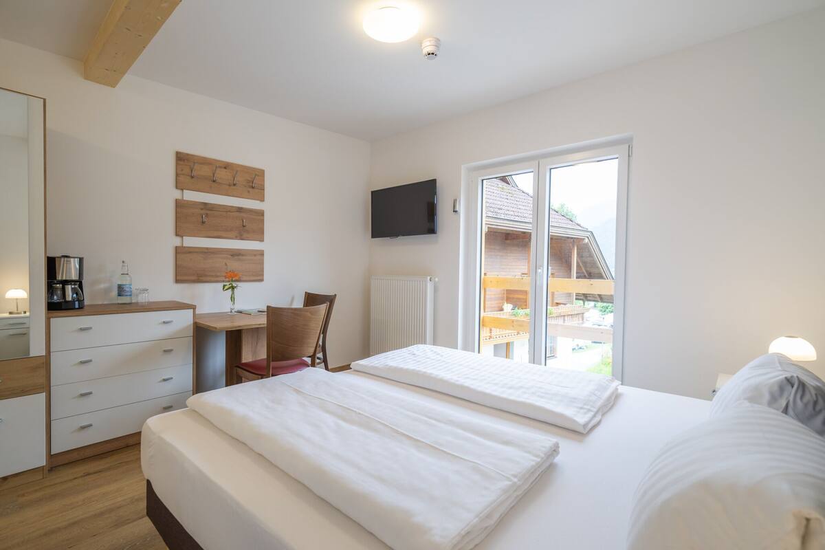 Habitación de hotel con cama, escritorio, silla, televisión y vistas al exterior.