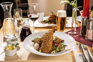 A dining table with a plate of food, including a breaded chicken leg, salad, and a glass of beer. There are also several glasses and a pitcher of water on the table. - Wellness Landhaus PARTH (Ossiach)