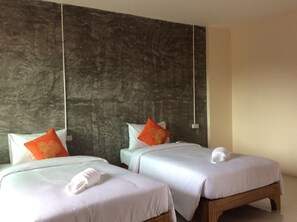 Two single beds with white bedding and orange pillows, a wooden headboard, and a textured gray wall.