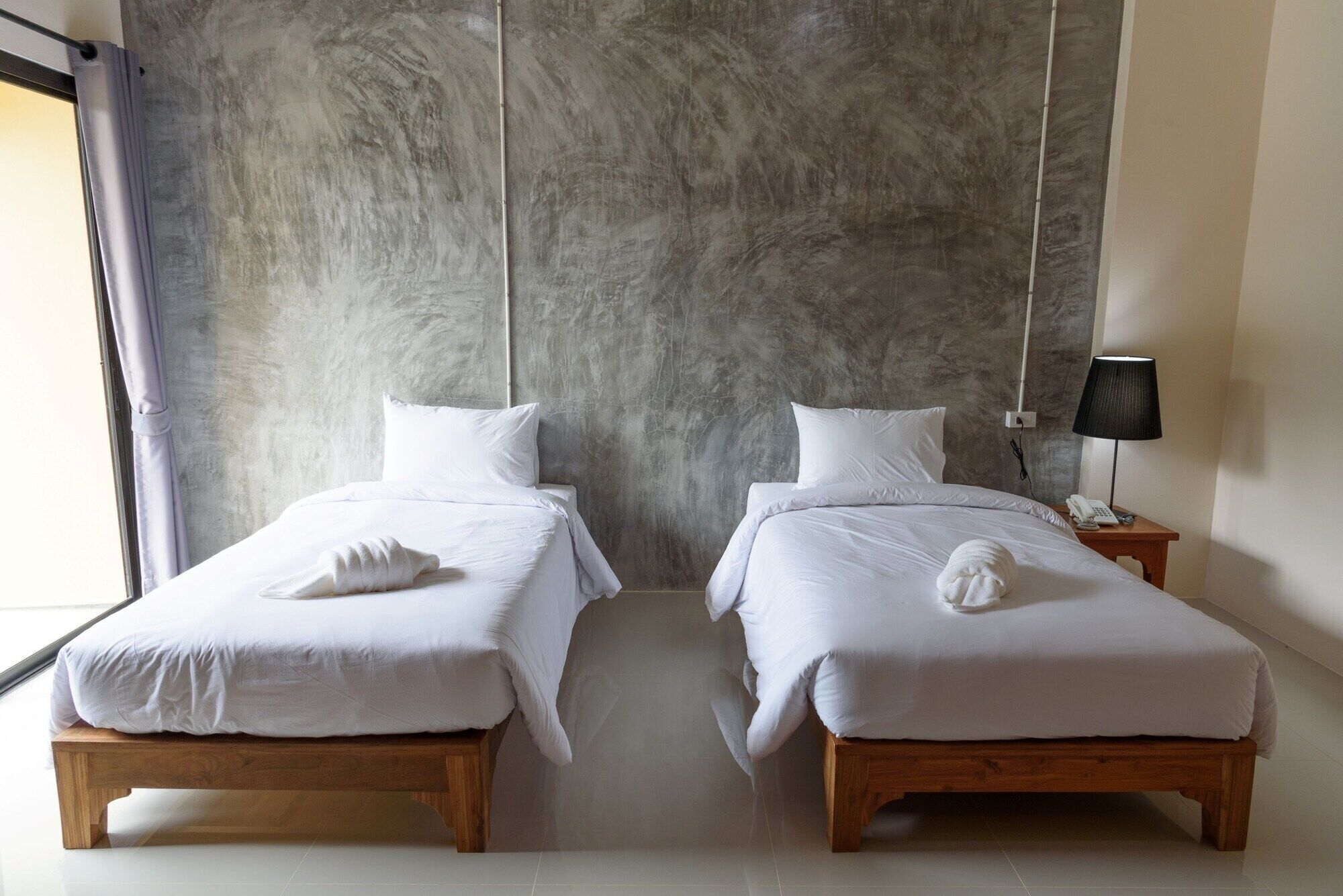Ein Hotelzimmer mit zwei Holzbett, weißer Bettwäsche und einer grauen Wand mit Struktur.