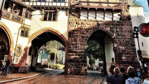 Un edificio histórico con una imponente torre del reloj, fachada tradicional de entramado de madera y un arco de piedra.