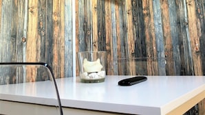 A room with a mounted TV on a wooden wall, a white desk with a glass container holding white objects, and a black remote control. - Deluxe Studio 9 in der Stadt (Freiburg im Breisgau)