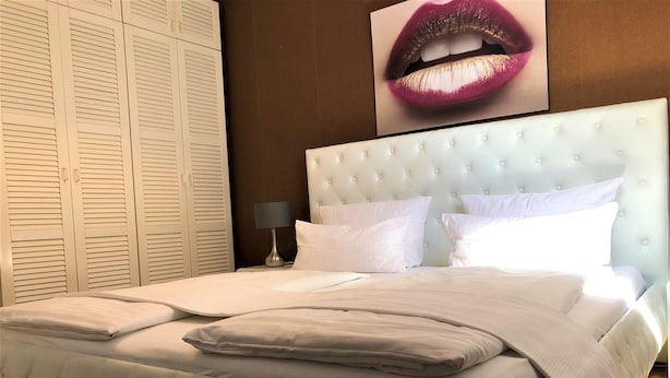 A neatly made bed with white linens and a tufted headboard, a bedside lamp, and a large framed picture of lips on the wall. - Deluxe Studio 9 in der Stadt (Freiburg im Breisgau)