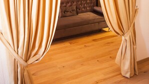 Une pièce avec un plancher en bois, un canapé marron et des rideaux beige noués en bas.