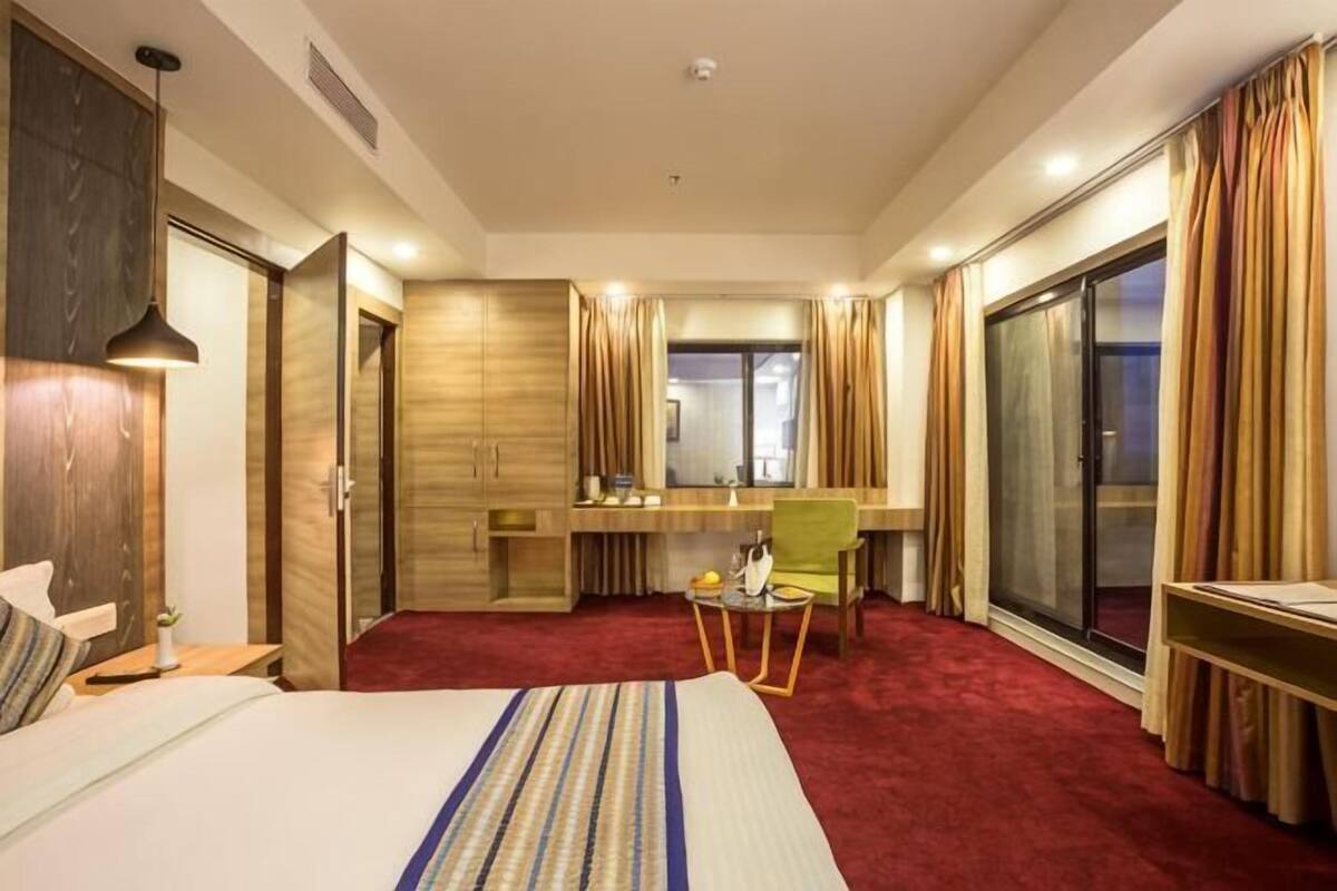 A hotel room with a bed, desk, chair, and large windows.