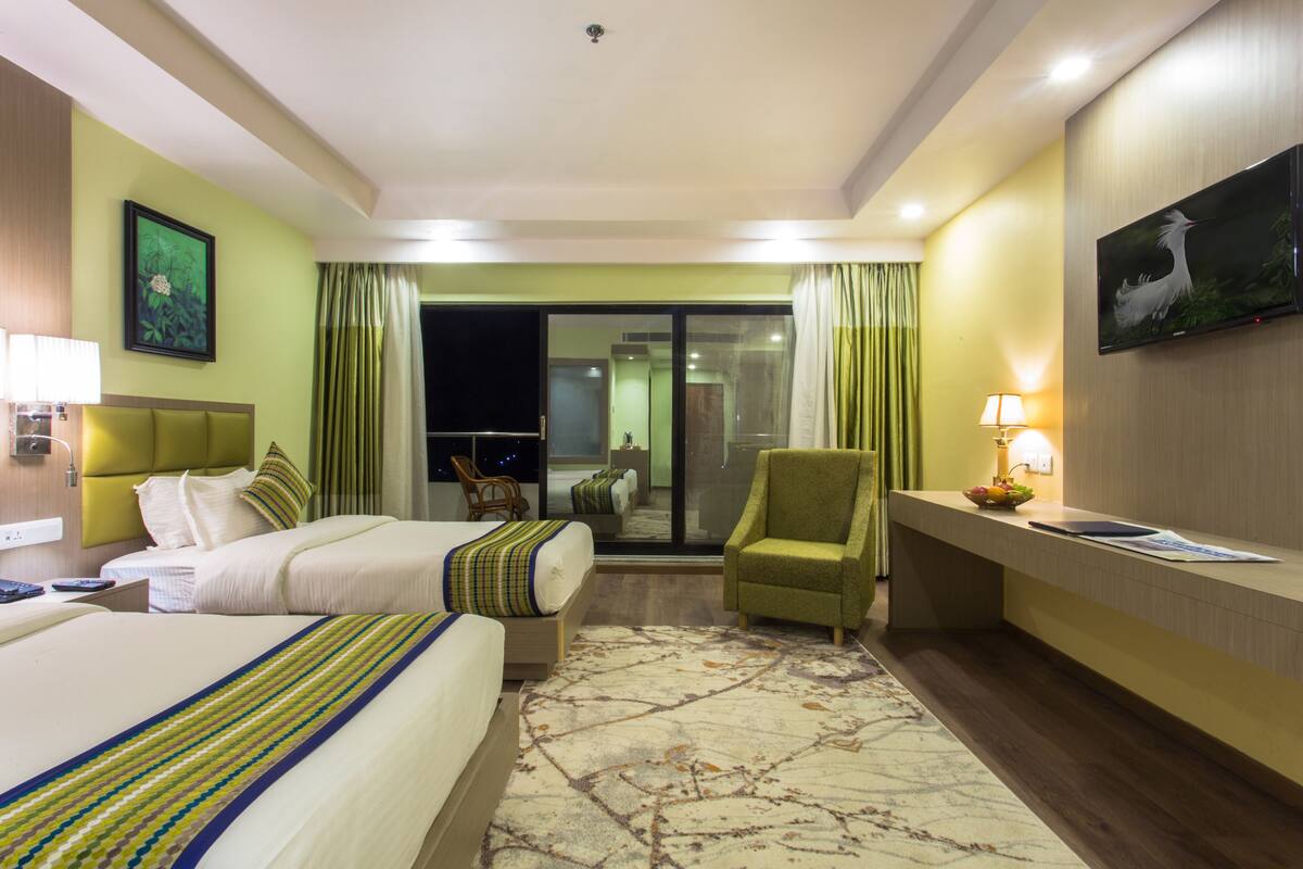 A hotel room with two beds, a desk, a chair, a TV, and a view of the outside.