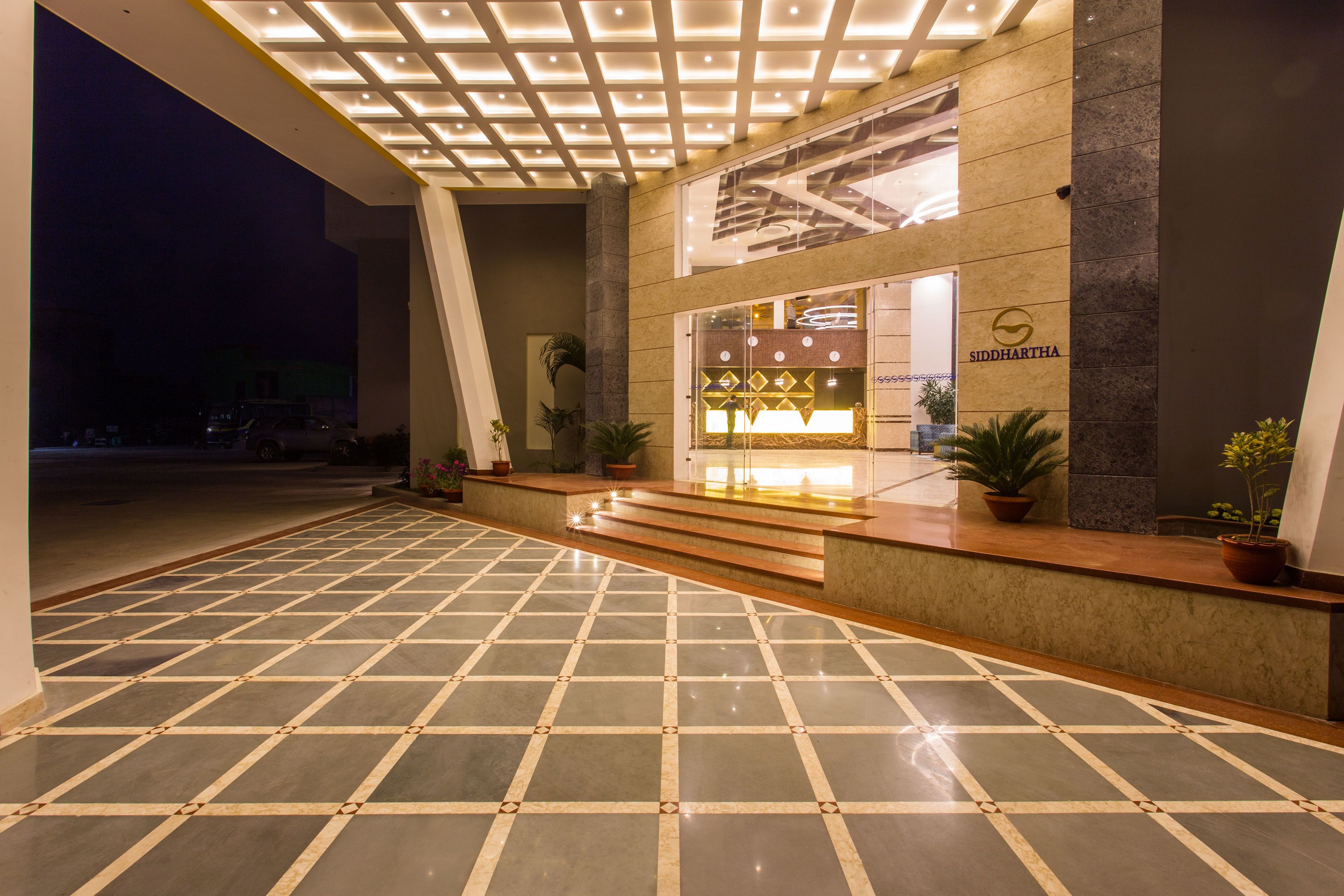 Un vestíbulo de hotel con piso de baldosas, una recepción y una escalera que sube a los pisos superiores.