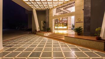 Un vestíbulo de hotel con piso de baldosas, una recepción y una escalera que sube a los pisos superiores.