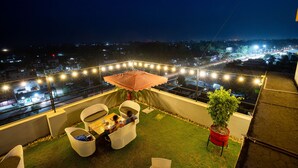 Eine Dachterrasse mit Essbereich, Lichterketten und Blick auf die beleuchtete Stadt bei Nacht.