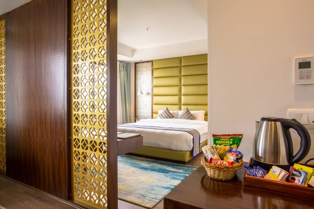 A hotel room with a bed, a coffee maker, a basket of snacks, and a kettle on the table.