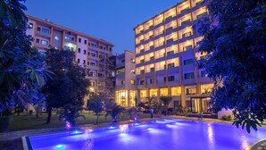 Ein modernes Hotel mit Schwimmbad, umgeben von üppiger Vegetation und warm beleuchtet.