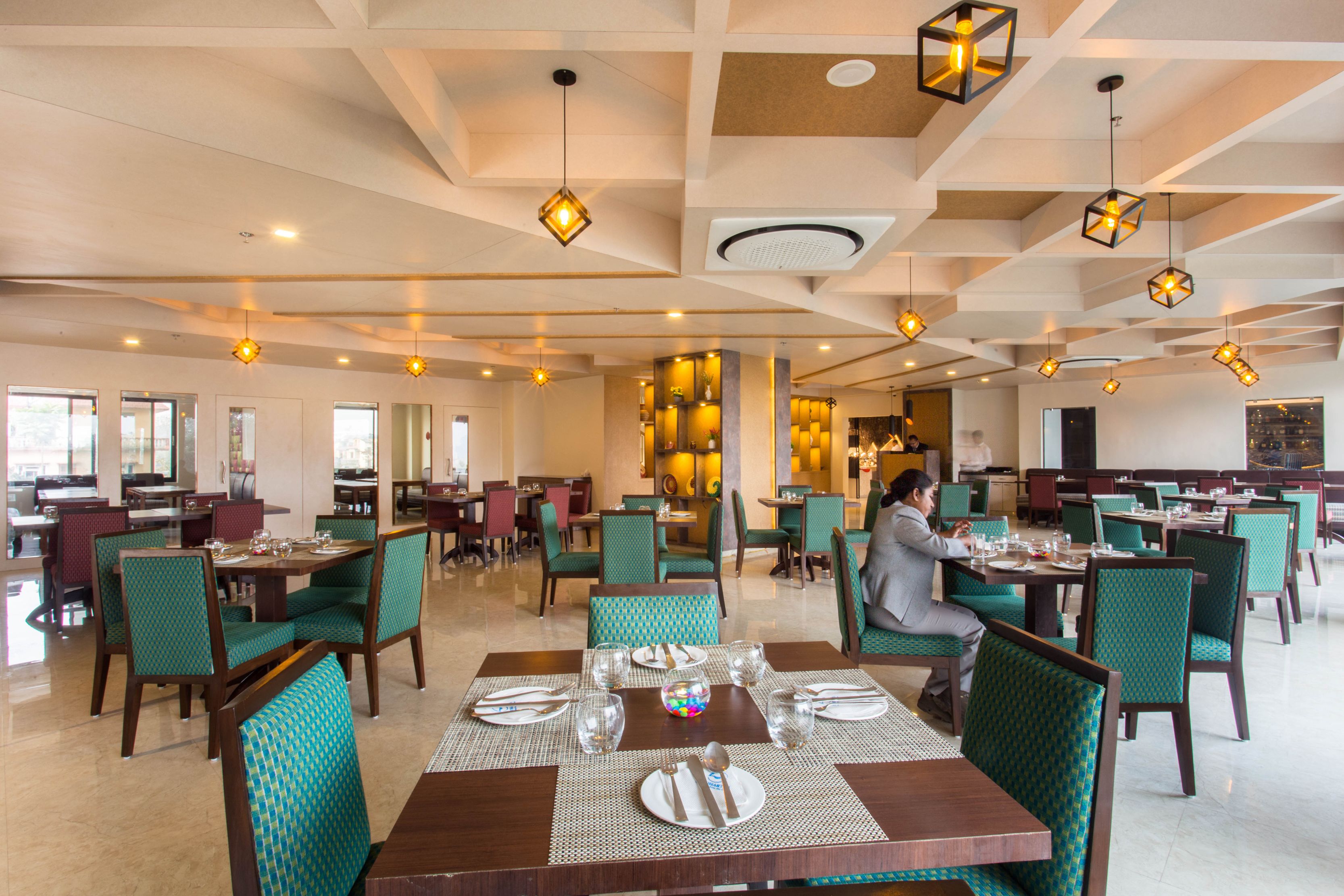 A spacious restaurant with multiple dining tables and chairs, featuring a modern ceiling design and pendant lighting.