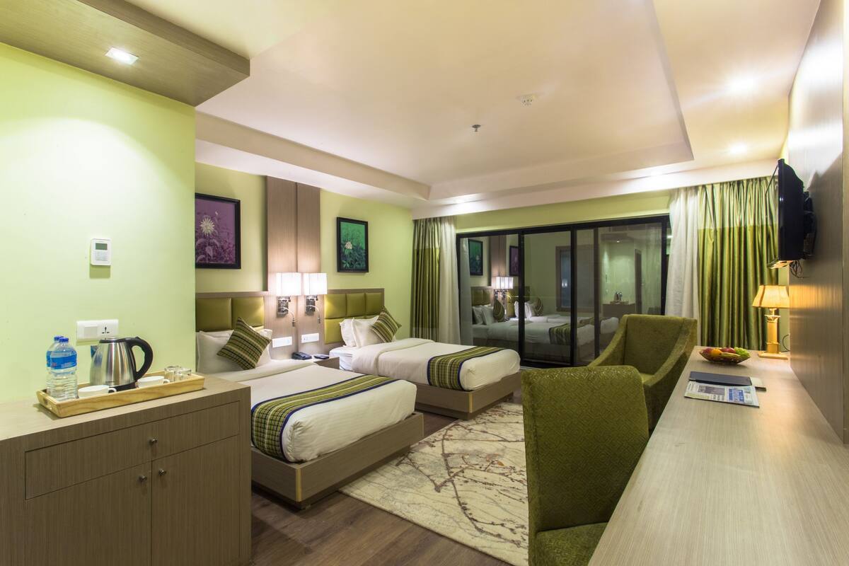 A hotel room with two beds, a desk, a chair, a TV, and a window with curtains.