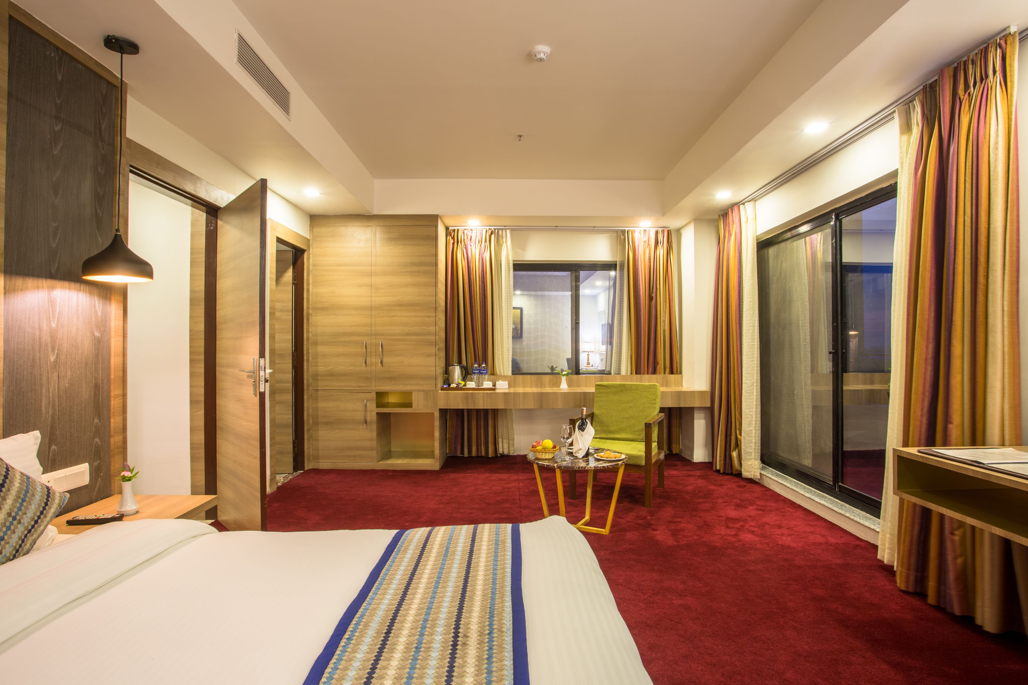 A hotel room with a large bed, a desk with a chair, a small table with a basket, and a sliding glass door.