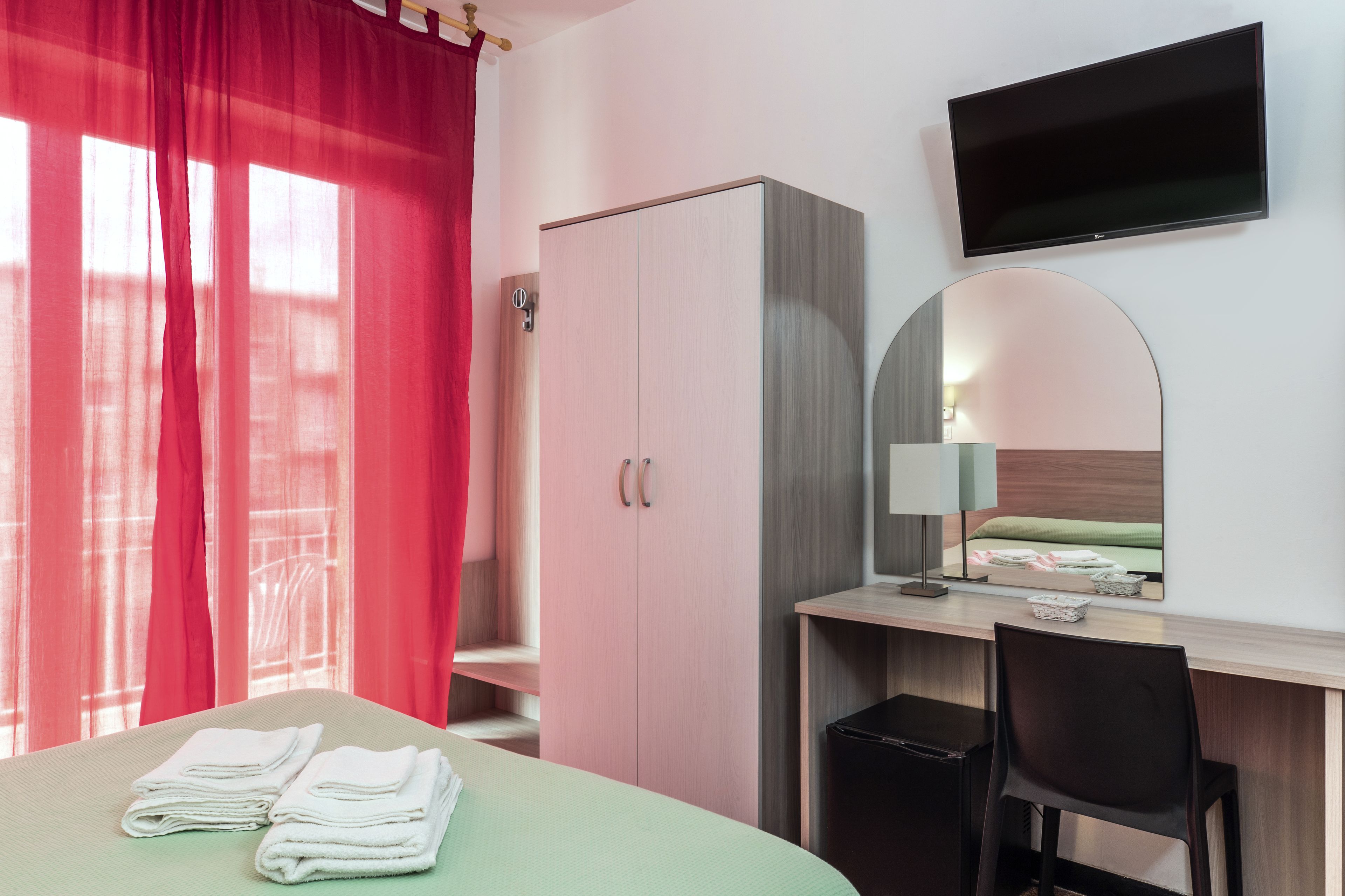 Una habitación de hotel con cama, escritorio, silla, armario, televisor y espejo.
