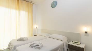 A hotel room with two beds, a bedside table with a phone, and a wall clock.