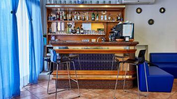Una zona de bar con mostrador de madera, estanterías llenas de botellas de licor, dos taburetes y un sofá azul.