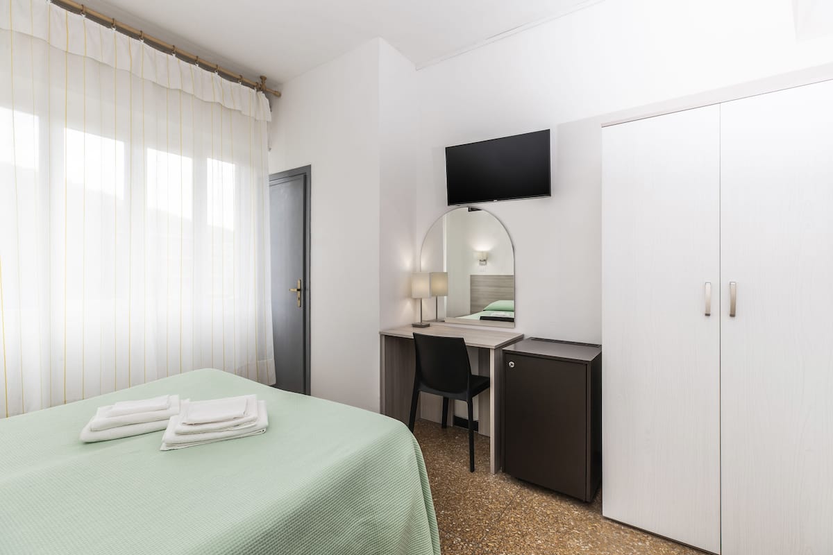 Ein Hotelzimmer mit Bett, Schreibtisch, Stuhl, Fernseher und Kleiderschrank.