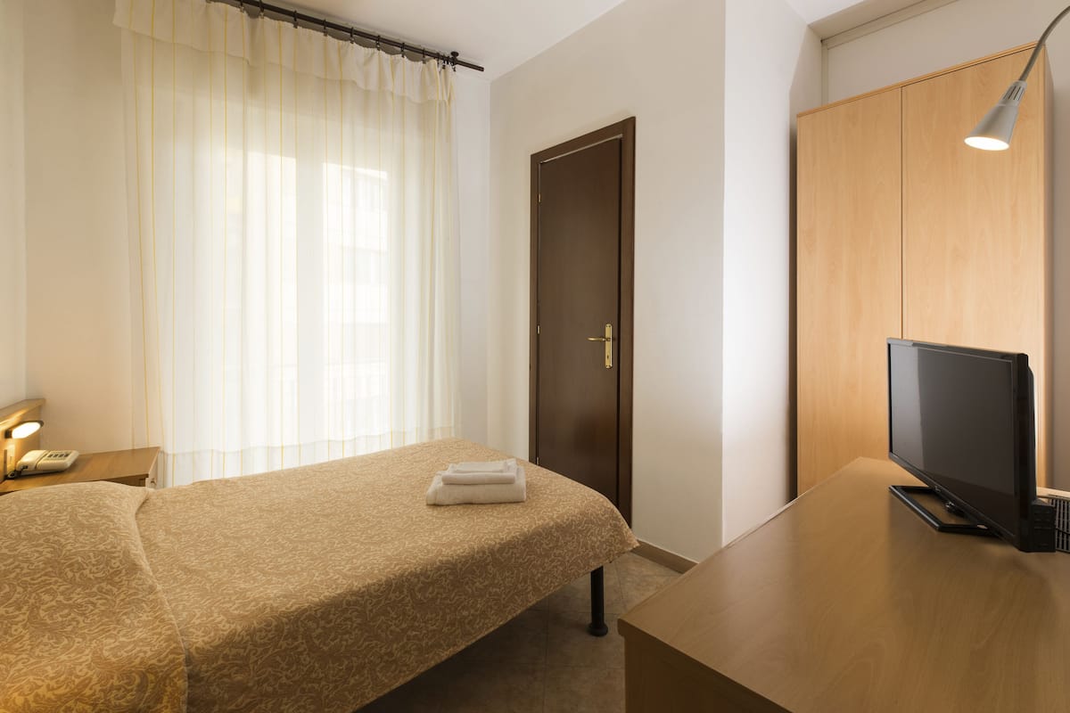 Ein Hotelzimmer mit einem Bett, einem Fernseher auf einem Holztisch, einer Tür und einem Vorhangfenster.