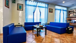 Un vestíbulo de hotel con sofás azules, una mesita y una zona de bar con estantes llenos de botellas.