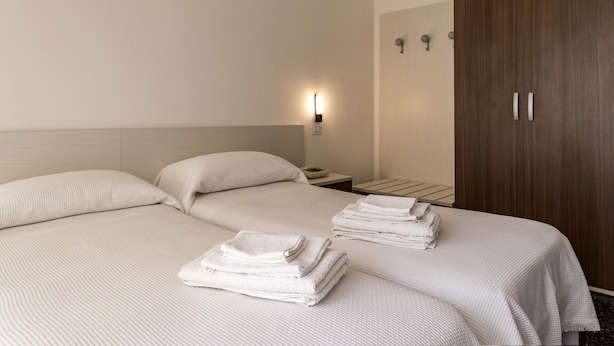 Habitación de hotel con dos camas, un armario de madera y una mesita de noche con lámpara.
