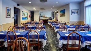 Un restaurante con varias mesas y sillas, una barra alargada y vistas al mar a través de las ventanas.