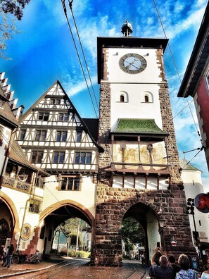 A historic building with a clock tower, a traditional half-timbered facade, and a stone archway. - New England Apartment (Freiburg im Breisgau)
