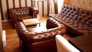 A living room with a brown leather sofa, a matching ottoman, and a wooden coffee table. The room has striped wallpaper and a patterned wall. - New England Apartment (Freiburg im Breisgau)