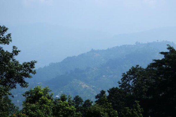 A mountainous landscape with dense forestation in the foreground and a hazy view of hills in the background.