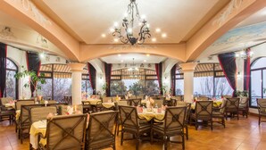 A restaurant with multiple tables and chairs, large windows, and a chandelier. - Mirabel Resort (Dhulikhel)